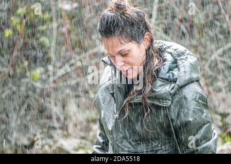 Jeune latina femme roulant sous une forte pluie avec vert trempé veste et cheveux qui s'égouttent Banque D'Images