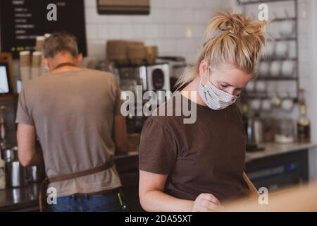 Serveuse blonde portant un masque de visage travaillant dans un café. Banque D'Images