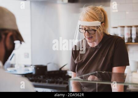 Serveuse blonde portant un masque de visage travaillant dans un café. Banque D'Images