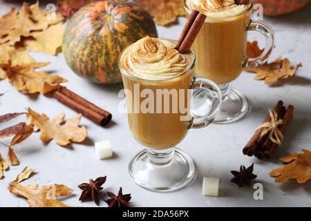 Deux tasses en verre de latte de citrouille aux épices et mousse crémeuse sur fond gris avec citrouilles et feuilles d'automne. Gros plan. Banque D'Images