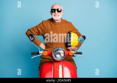 Portrait de son beau funky attrayant gai contenu de la gaie cool barbu gris-cheveux homme hippster assis mobylette service de location isolé sur bleu Banque D'Images