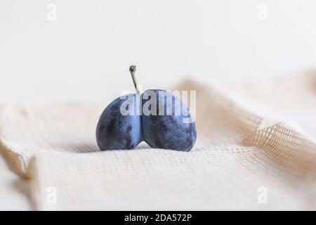 Bleu biologique laid prunes double coeur en forme de coeur sur un fond blanc. La mauvaise tendance des produits est la vente de produits imparfaits. Banque D'Images