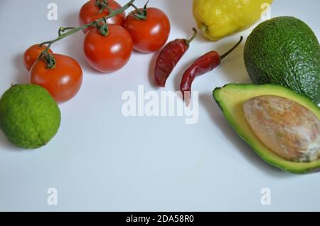 Ingrédients pour guacamole sur fond blanc. Tomates cerises, piments, avocats, ingrédients pour la cuisine mexicaine. Banque D'Images