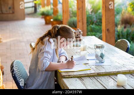 Une adolescente écrit dehors sur la terrasse au coucher du soleil. Banque D'Images