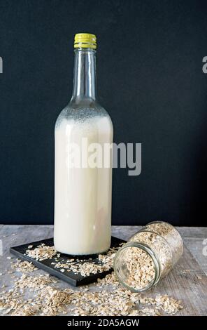 Lait d'avoine vegan dans un grand biberon avec de l'avoine qui déborde de pot sur carreau noir sur fond noir Banque D'Images