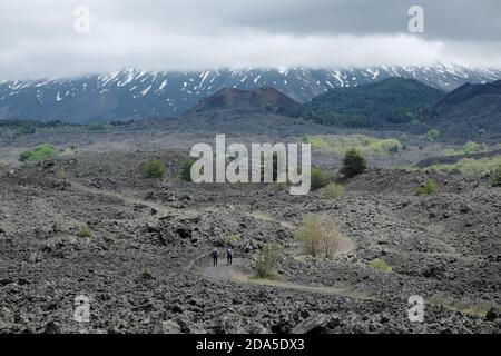 Couple randonneurs sur le chemin des cônes de cendres éteints sous le majestueux cône volcanique de l'Etna Mount qui est couvert de nuages, la Sicile Banque D'Images