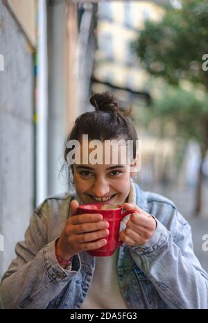 Jeune femme buvant d'une tasse une terrasse regardant appareil photo et sourire Banque D'Images