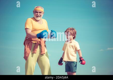 Portrait d'un boxeur senior déterminé avec un petit garçon enfant sur fond bleu ciel. Boxer grand-père et enfant avec gant de boxe bleu sur ciel bleu Banque D'Images