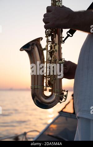 Musicien de jazz jouant sur saxophone au bord de la mer au coucher du soleil Banque D'Images