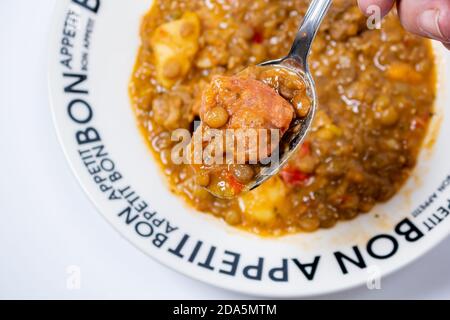 Ragoût maison de lentilles, de tomates, de chorizo espagnol, de viande et de pommes de terre servi dans un plat profond avec un motif noir sur une surface blanche. Vue Zenital Banque D'Images