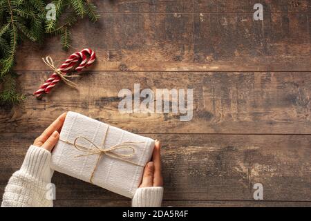 Noël présent boîte cadeau dans les mains de la femme sur fond rustique en bois. Branches de l'arbre de Noël et canes de bonbons sur l'ancienne table en bois Banque D'Images