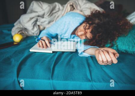 La femme caucasienne couchée somnolent dans le lit est en train de lire quelque chose de un livre portant un pyjama bleu tard dans la nuit Banque D'Images