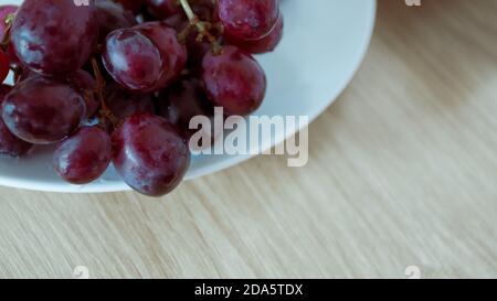 Gros plan de raisins avec des gouttelettes d'eau sur une plaque en céramique blanche. Banque D'Images