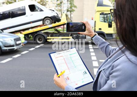 Une femme agent remplit une police d'assurance après un accident de voiture et enregistre une vidéo sur un smartphone. Banque D'Images