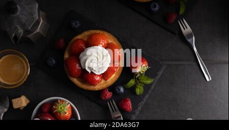 Tarte aux fraises bio maison à la framboise et aux baies bleues avec café sur fond sombre vue du dessus. Banque D'Images