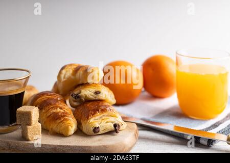 Petit-déjeuner avec croissants, petits pains à la cannelle et biscuits au chocolat, jus d'orange frais et café sur le côté sur fond blanc. Banque D'Images