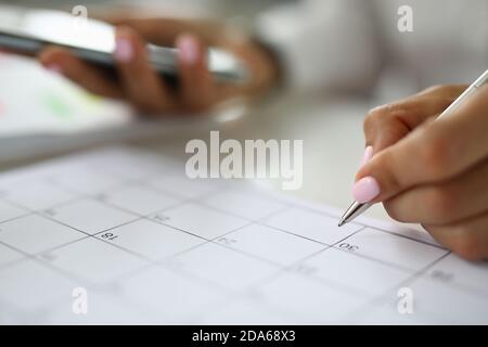 La main de la femme tient le stylo et le calendrier des marques. Banque D'Images