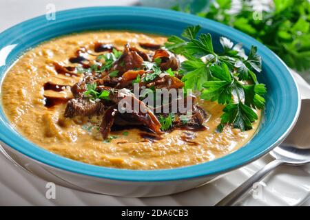 Soupe crémeuse de potiron avec bouillon de champignons sauvages et lait de coco garni de graines de sésame et de persil frais servi sur un bol bleu avec sauce soja sur un li Banque D'Images