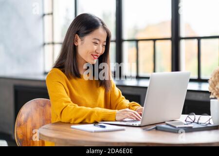 Femme asiatique travaillant sur un ordinateur portable à la maison ou dans un café. Jeune femme en jaune vif cavalier Banque D'Images