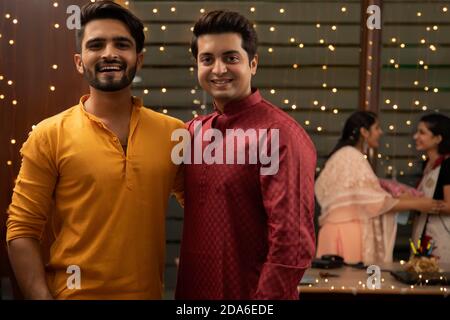 DEUX COLLÈGUES MASCULINS REGARDANT LA CAMÉRA ET POSANT AVEC UNE FEMME SES COLLÈGUES SE FONT DES CADEAUX EN ARRIÈRE-PLAN Banque D'Images