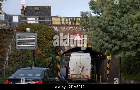 Lower Downs Road, Wimbledon, Londres, Royaume-Uni. 10 novembre 2020. Un rapport de Network Rail montre que ce pont ferroviaire de Wimbledon est l'un des « plus bashed » de Londres, arrivant au 2e et frappé 11 fois en 2019-20. Il est également le 10e plus égal de bashed en Grande-Bretagne. Au-dessus de cet étroit pont voûté se trouvent quatre voies ferrées, deux pour les trains de banlieue et deux pour les trains express à destination et en provenance de Londres Waterloo au sud-ouest de l'Angleterre. Le panneau du parapet de Low Bridge est partiellement masqué par le feuillage des arbres à l'approche sud. Crédit : Malcolm Park/Alay Live News. Banque D'Images