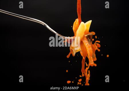 un filet de sauce tomate tombe sur une fourchette avec les pâtes créent de nombreuses éclaboussures sur un fond noir Banque D'Images