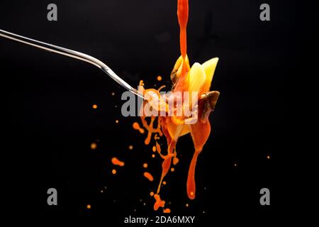 un filet de sauce tomate tombe sur une fourchette avec le pâtes créant de nombreuses éclaboussures sur un fond noir Banque D'Images