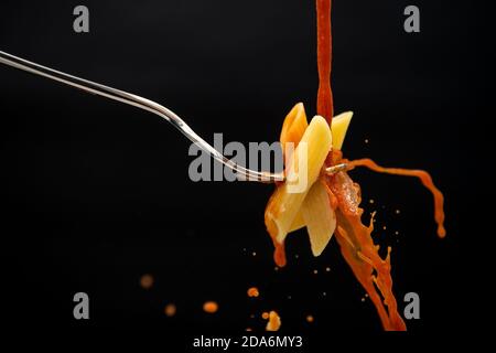 un filet de sauce tomate tombe sur une fourchette avec les pâtes créent de nombreuses éclaboussures sur un fond noir Banque D'Images