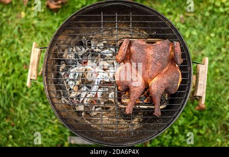 Poulet traditionnel au barbecue spatchcoké et mattone sur le grill au charbon de bois. Griller et fumer du poulet à la craque en plein air sur du bois de chauffage barbecue grill en natu Banque D'Images