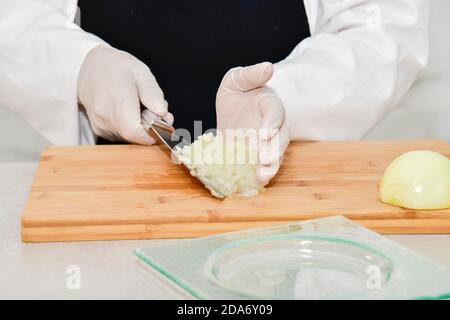 Gros plan de l'oignon haché saisi par un chef hors foyer avec l'aide d'un couteau de cuisine. Concept de sécurité et de cuisson. Banque D'Images