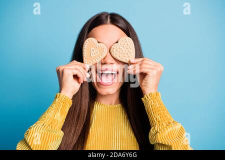 Photo portrait d'une fille excitée couvrant deux yeux en forme de coeur biscuits au pain d'épice isolés sur fond bleu pastel Banque D'Images