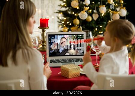Une famille heureuse avec un enfant fête Noël avec ses amis lors d'un appel vidéo à l'aide d'une webcam. La veille de Noël, la famille accueille leurs parents Banque D'Images