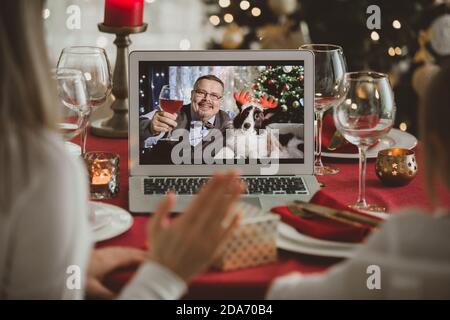 Une famille heureuse avec un enfant fête Noël avec ses amis lors d'un appel vidéo à l'aide d'une webcam. La veille de Noël, la famille accueille leurs parents Banque D'Images