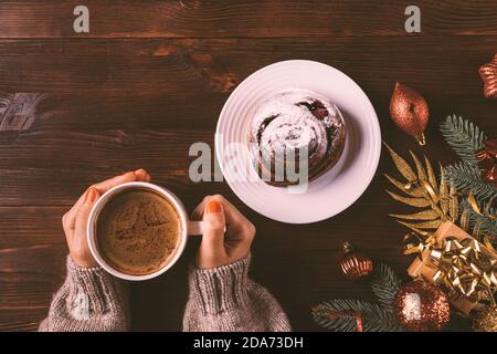 Composition de Noël à plat les mains des femmes tenant une tasse de café à côté d'un petit pain maison, de branches de sapin, de boules rouges et d'une boîte cadeau sur fond de bois. Banque D'Images