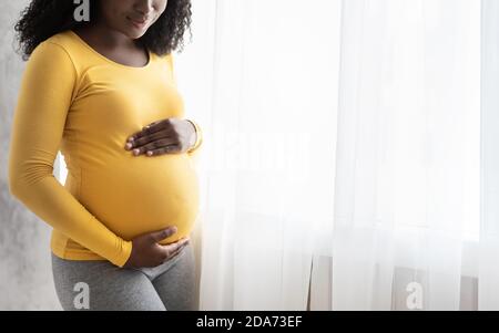 Écourté de femme enceinte noire debout près de la fenêtre Banque D'Images