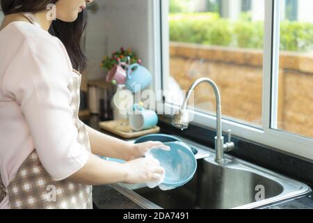 Image rognée d'asiatique belle jeune femme est de laver la vaisselle dans l'évier dans la cuisine tout en faisant le nettoyage à la maison Banque D'Images