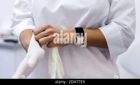 Une jeune femme dentiste met des gants en latex blanc Banque D'Images