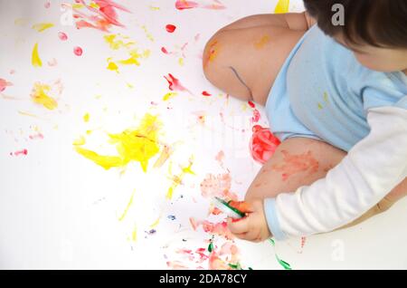 bébé heureux tire avec des peintures de couleur les mains, les doigts et les paumes sont colorés avec de la peinture. Banque D'Images