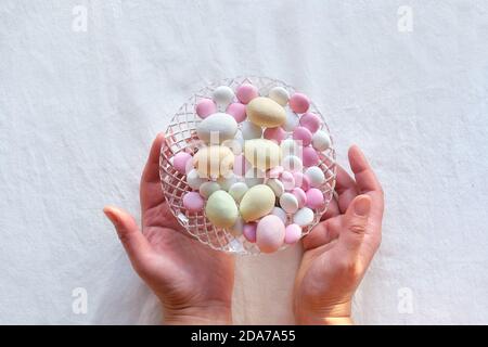 Les mains joyeuses Pâques montrent vase en verre de cristal avec des œufs de Pâques en massepain et des boutons de bonbons au chocolat. Banque D'Images