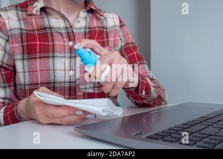 Femme mains pulvérisation antiseptique, nettoyage clavier d'ordinateur portable avec désinfectant humide essuie sur la table. Désinfection, protection, prévention, travaux ménagers, COVID Banque D'Images