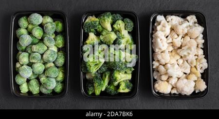 Ensemble de légumes surgelés dans des récipients sur fond noir. Choux de Bruxelles, chou-fleur, brocoli. Vue de dessus, plan d'appartement. Banque D'Images