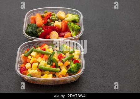 Légumes congelés dans des récipients en plastique sur fond noir. Copier l'espace. Mélange de salades de légumes. Vue latérale. Banque D'Images