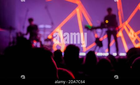 Arrière-plan de concert flou - les gens crossent la silhouette et applaudissent au concert de rock devant la scène de la discothèque. Rouge vif et coloré Banque D'Images