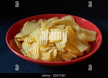 Les chips de pomme de terre dans une assiette rouge sur fond noir. Produits de l'alimentation en gros plan Banque D'Images