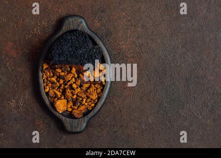 Champignons de chaga et morceaux de chaga hachés dans un plateau en bois sur fond brun foncé. Espace de copie, vue de dessus, Flat lay. Banque D'Images