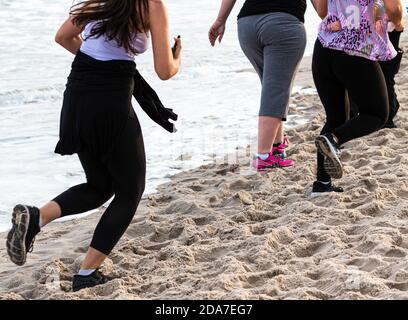 Vue de l'arrière en regardant vers le bas quelques femmes marchant et courir sur le bord de la plage à proximité de la de l'eau portant du spandex en début de soirée pendant les 3 s. Banque D'Images