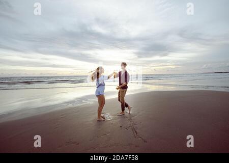 Couple jouant et dansant sur la plage, en riant. Coucher de soleil sur une plage à Bali, Indonésie Banque D'Images