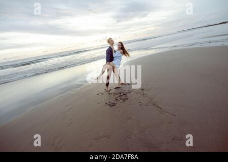 Couple jouant et dansant sur la plage, riant.coucher de soleil sur une plage à Bali, Indonésie Banque D'Images