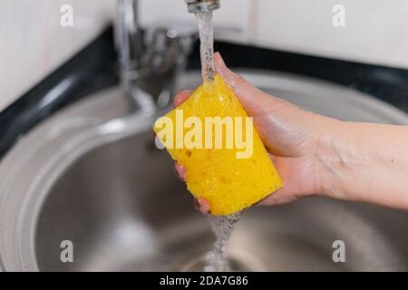 Éponge jaune pour les plats sous l'eau dans la main de fille Banque D'Images