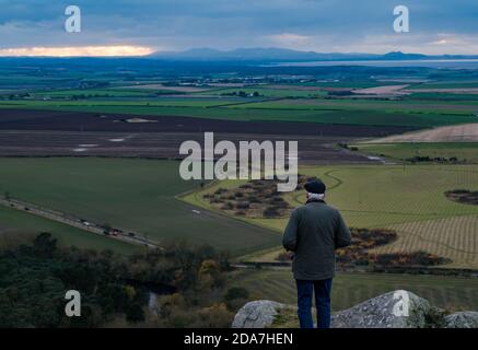 Berwick Law, East Lothian, Écosse, Royaume-Uni, 10 novembre 2020. Météo au Royaume-Uni : vue au crépuscule depuis le sommet de la loi de Berwick, une prise volcanique, un jour couvert. Un homme âgé regarde la vue Ouest à travers un paysage agricole vers le contour distinctif d'Édimbourg Banque D'Images